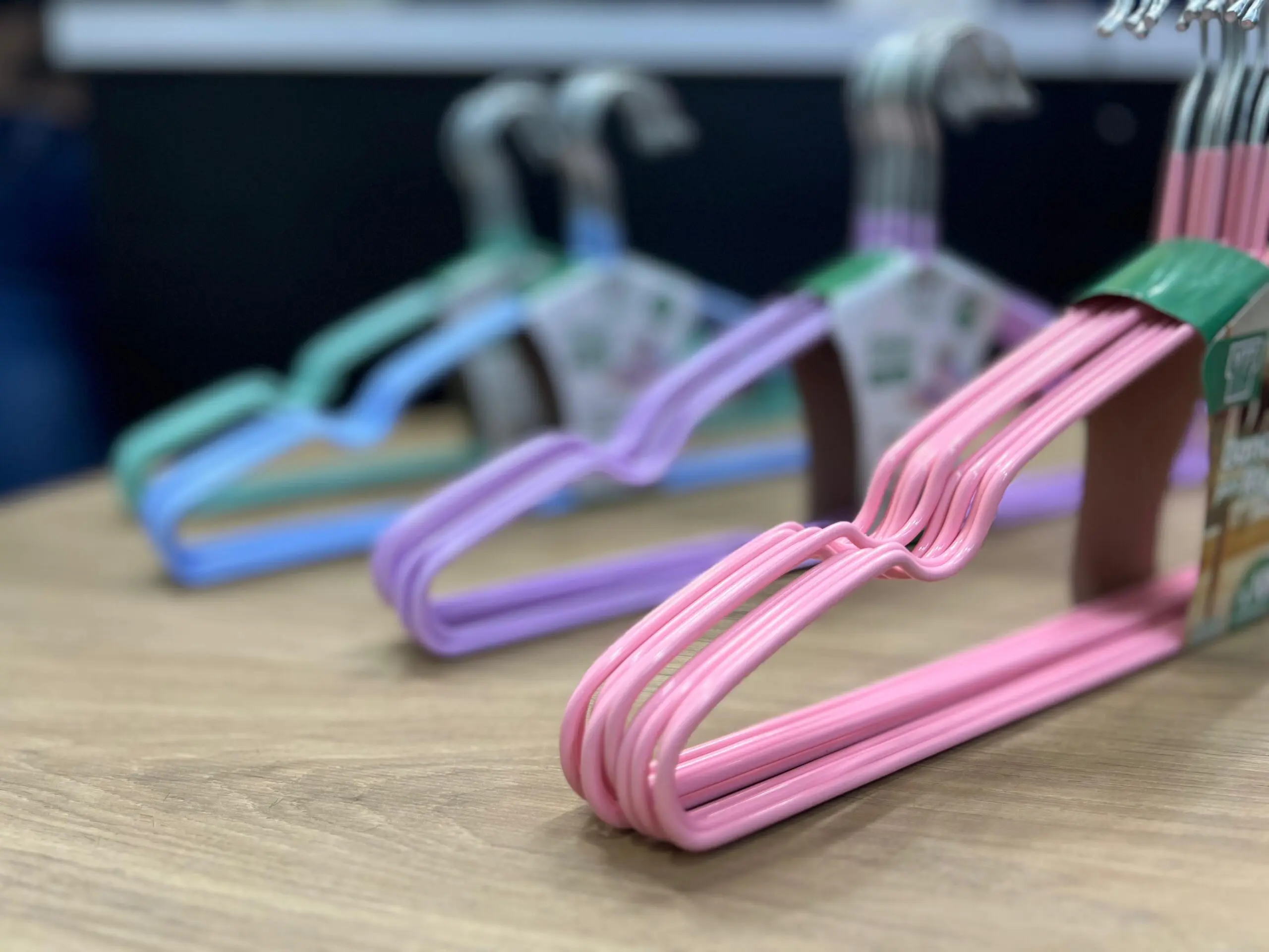 Sets de ganchos para ropa antideslizantes en colores rosa, morado, azul y verde, organizados en fila sobre una superficie de madera.