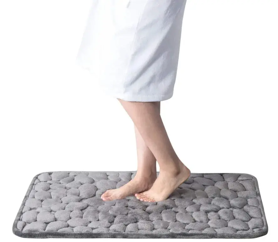 Tapete de baño gris con textura de piedras redondeadas en relieve, con pies descalzos para mostrar su suavidad y comodidad.