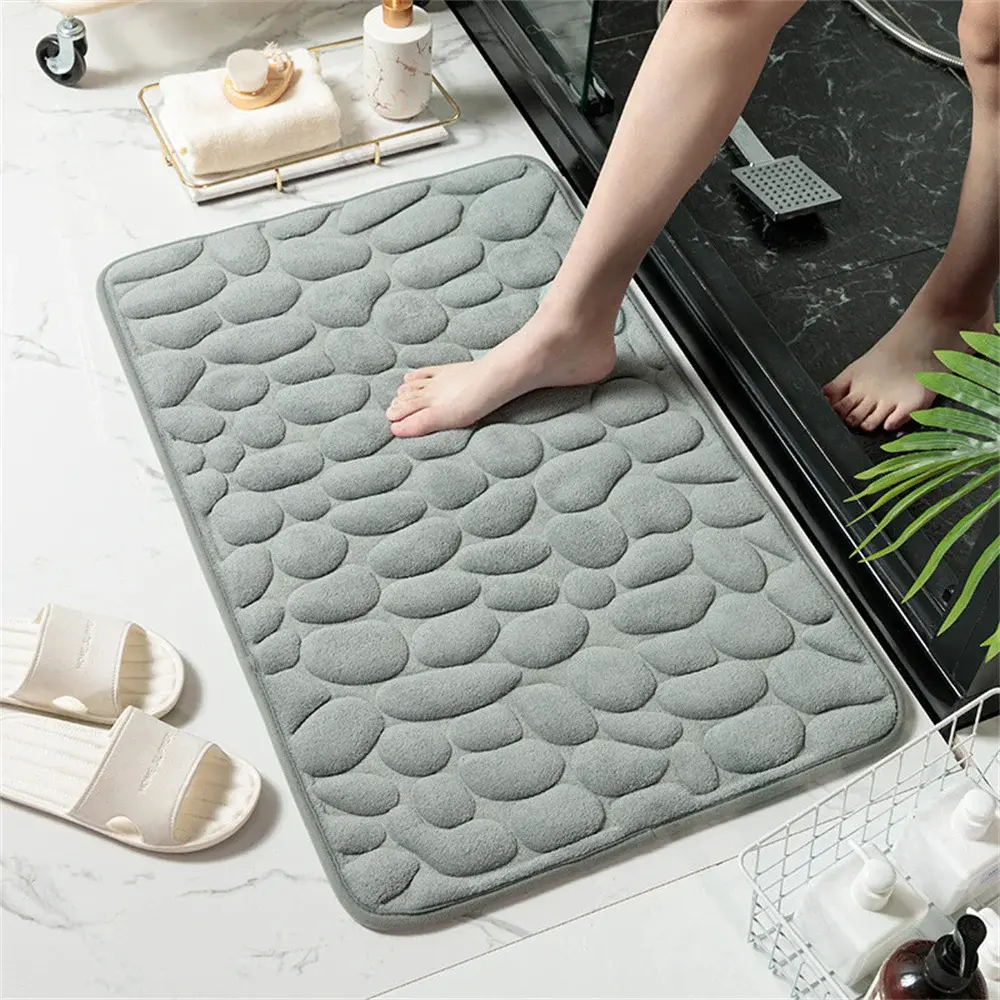 Tapete de baño gris con textura de piedras en relieve de espuma viscoelástica, usado al salir de la ducha sobre piso de mármol blanco.