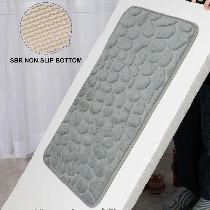 Tapete de baño gris con relieve de piedras y base antideslizante SBR beige, mostrado en ángulo para apreciar su textura y grosor.