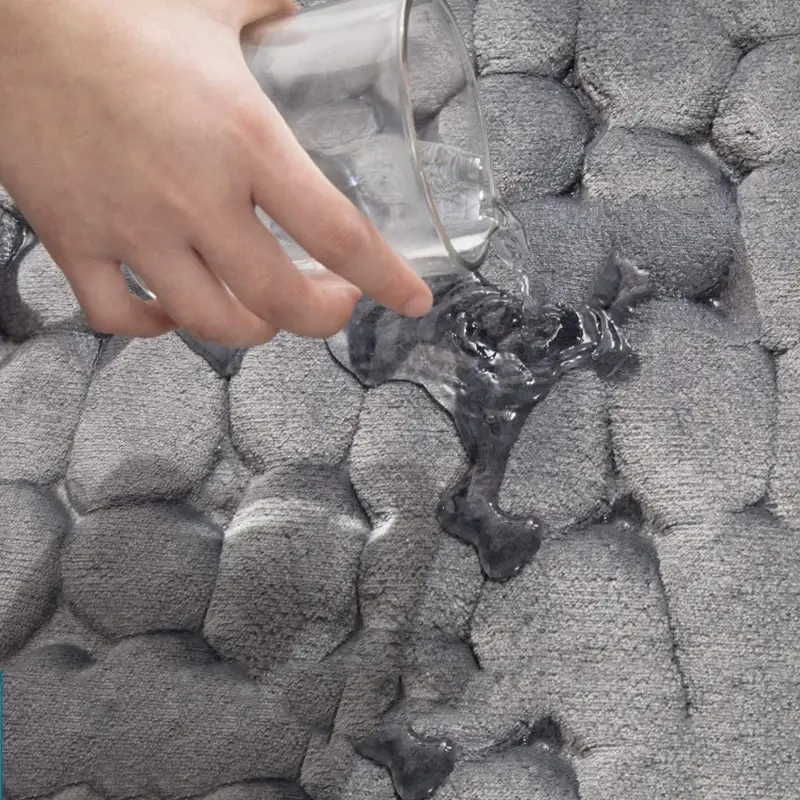 Mano vertiendo agua sobre tapete de baño gris de espuma viscoelástica con textura de relieve redondeado.
