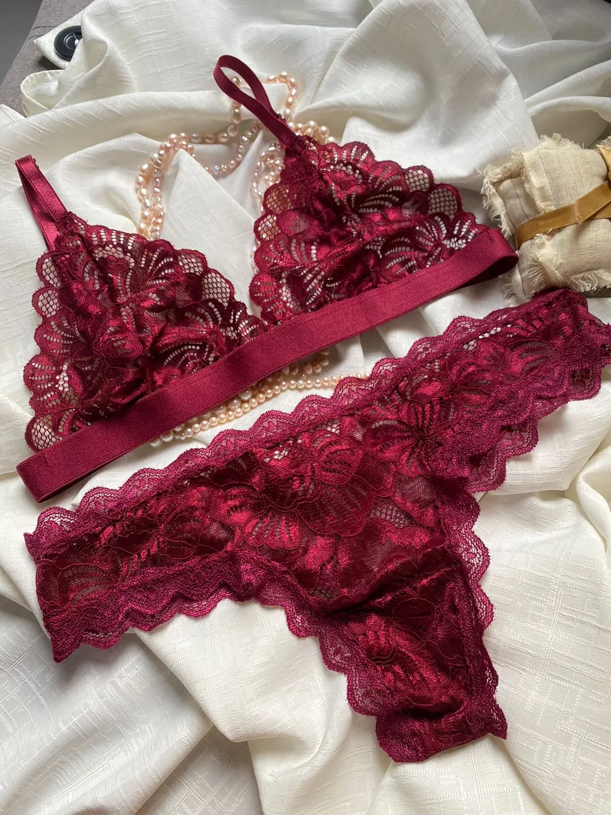 Conjunto de lencería color vino tinto en encaje floral con tirantes de satín, incluye bra y panty sobre tela blanca con perlas.