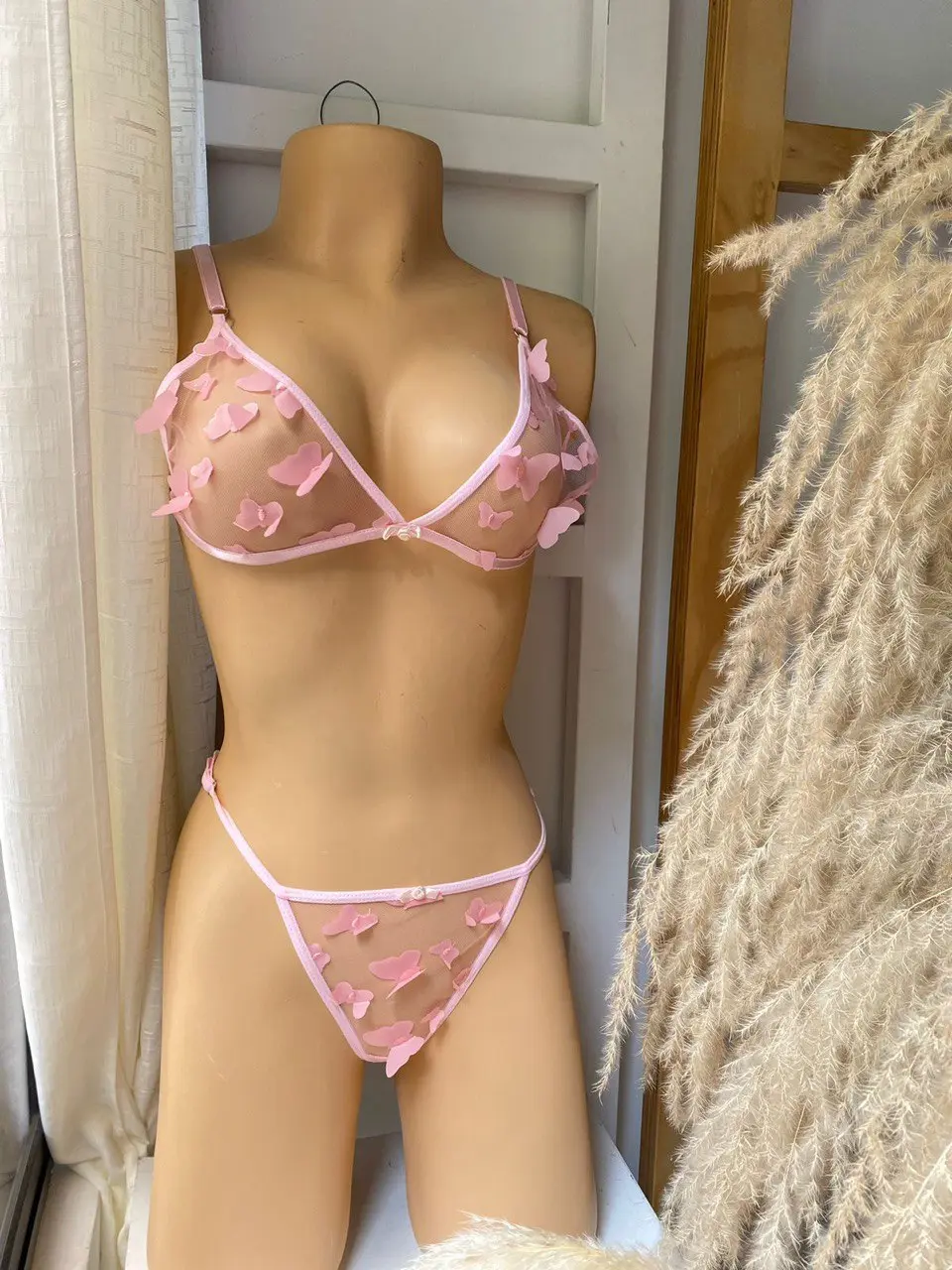 Conjunto lencería rosa sin varillas en maniquí, tela transparente con apliques de mariposas en relieve y tiras ajustables.