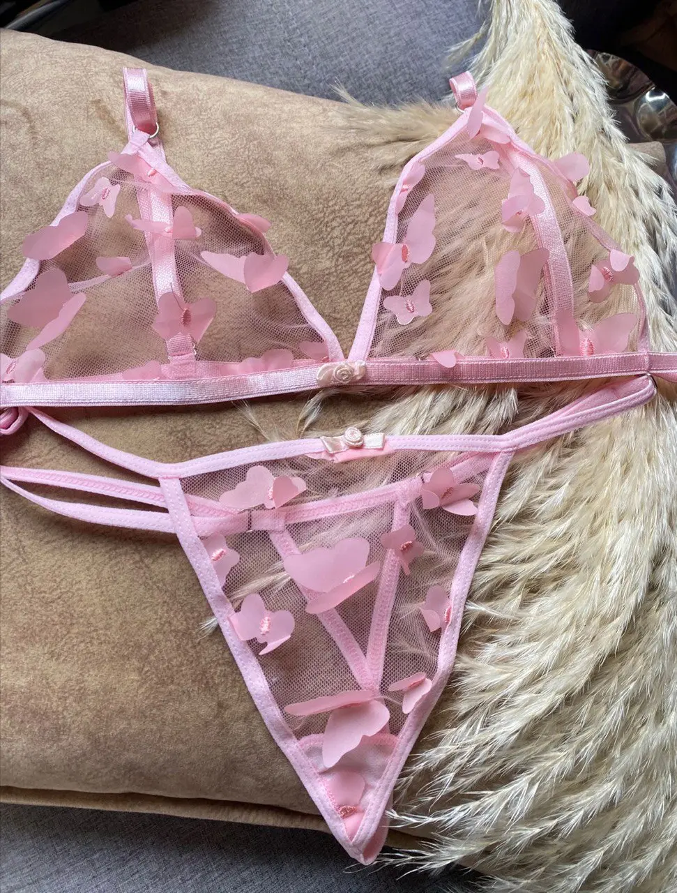 Conjunto rosa de lencería sin varillas en tul transparente con apliques de mariposas en 3D, incluye sujetador y tanga ajustable.