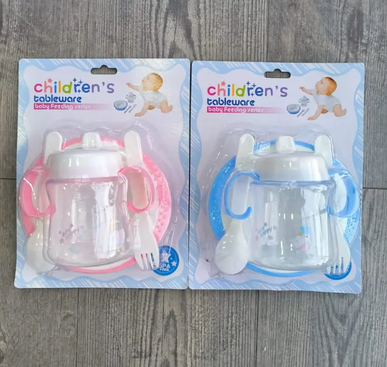 Dos sets de vajilla infantil de cuatro piezas en empaque plástico, uno rosa y otro azul, cada uno incluye plato, vaso antiderrame, cuchara y tenedor.