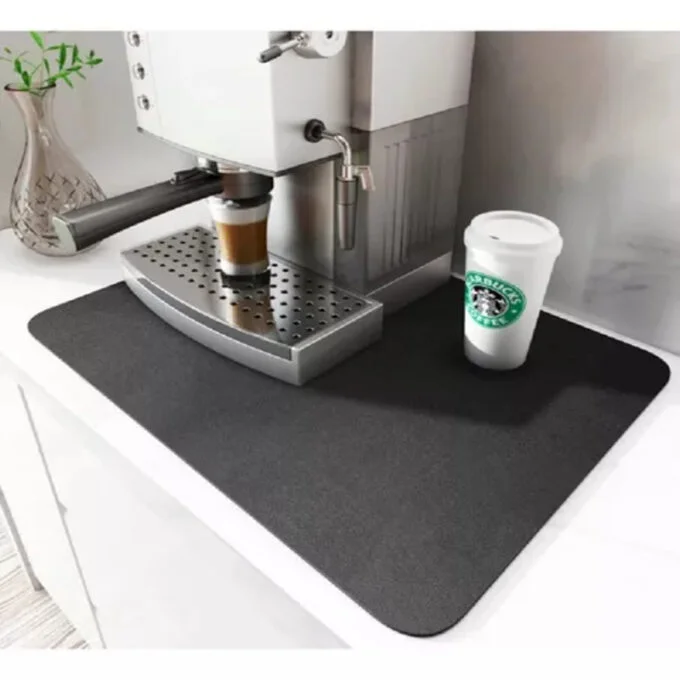 Tapete negro absorbente para cocina sobre encimera blanca, ubicado bajo una cafetera para proteger de manchas y humedad.