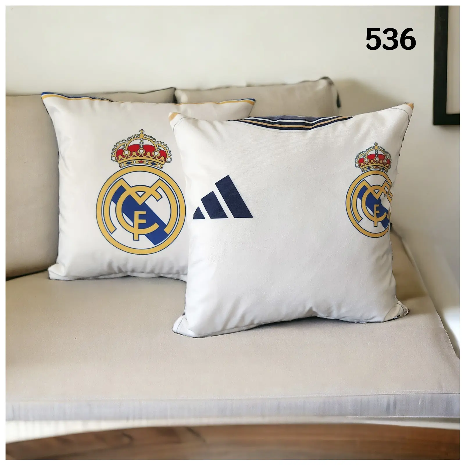 Set de dos fundas de cojín blancas con el escudo del Real Madrid y logo de Adidas, sobre un sofá color crema.