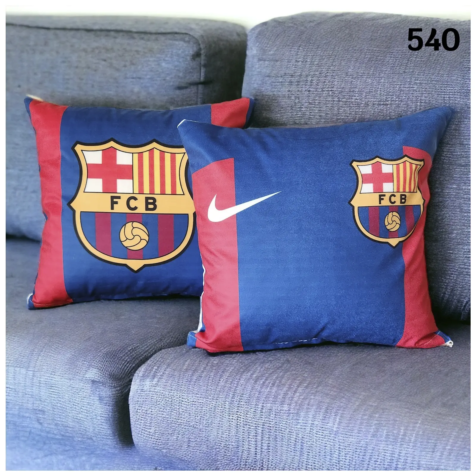 Dos fundas para cojines de fútbol inspiradas en el FC Barcelona, con diseño azul y grana, escudo y logo de Nike sobre sofá gris.