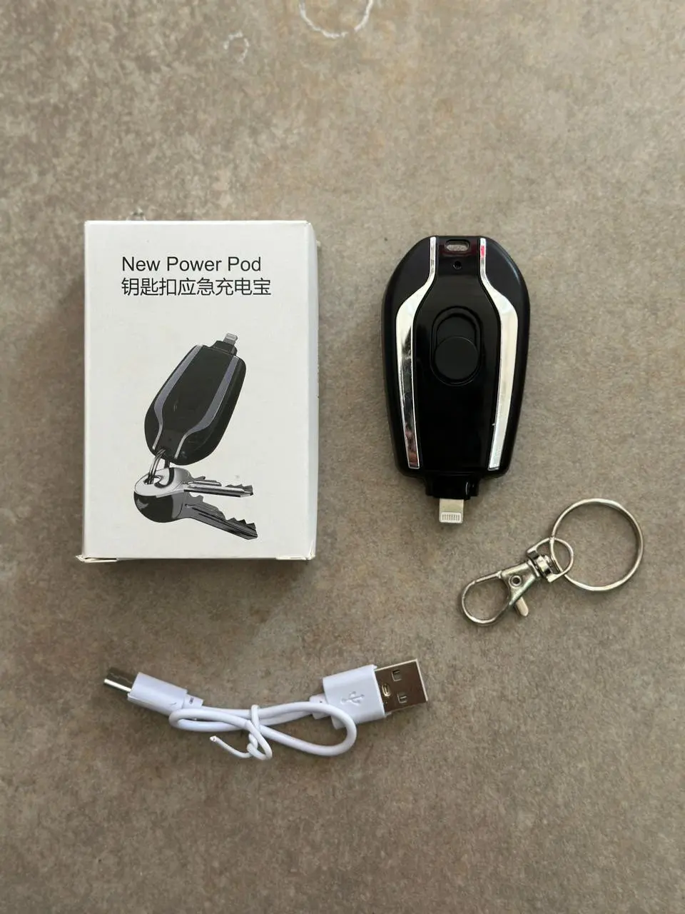 Cargador portátil negro de llavero para iPhone, con cable USB de carga, llavero metálico y caja blanca con texto.