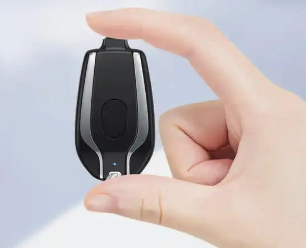 Cargador portátil para iPhone de llavero en color negro con detalles plateados, sostenido entre los dedos para mostrar su diseño compacto.