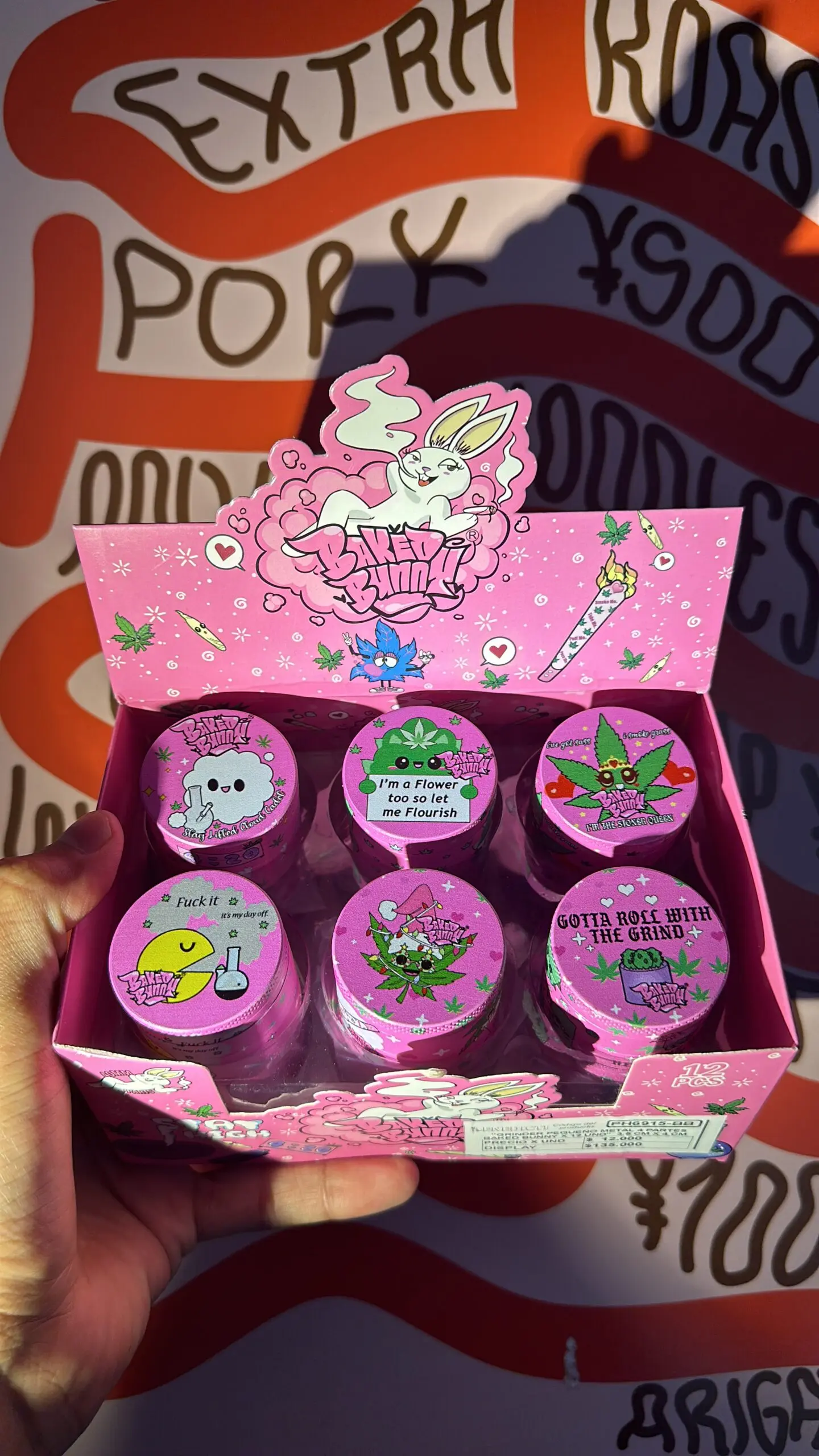 Caja expositora rosa con seis moledores de hierbas de tres pisos y tapas ilustradas con diseños animados variados de la marca Baked Bunny.
