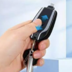 Mano sosteniendo llavero cargador portátil negro con conector desplegable superior y llavero metálico integrado.