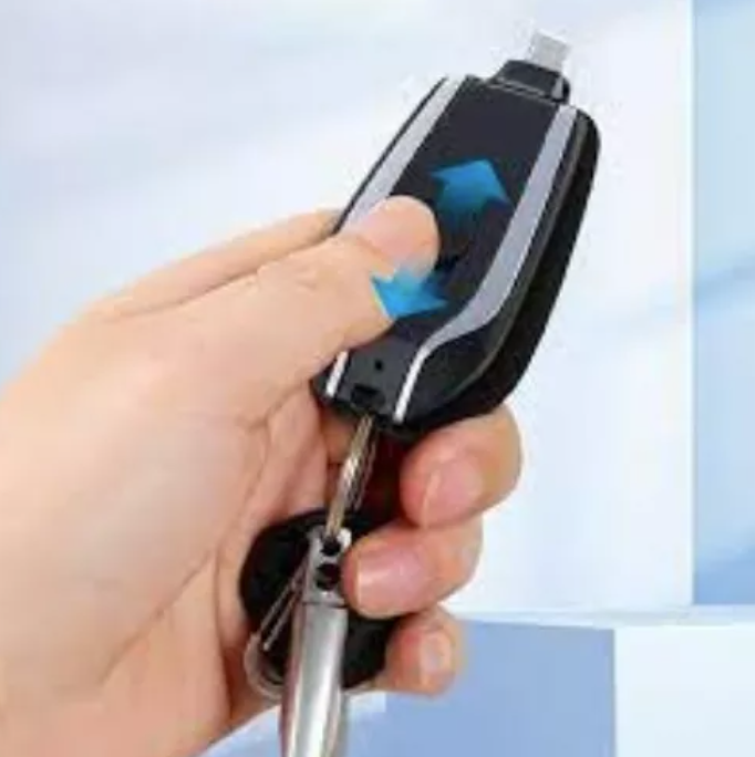 Mano sosteniendo llavero cargador portátil negro con conector desplegable superior y llavero metálico integrado.