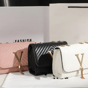 Tres bolsos de mano acolchados en colores rosado, negro y blanco, con costuras chevron, solapa frontal, herraje dorado en forma de V con borla y cadena.
