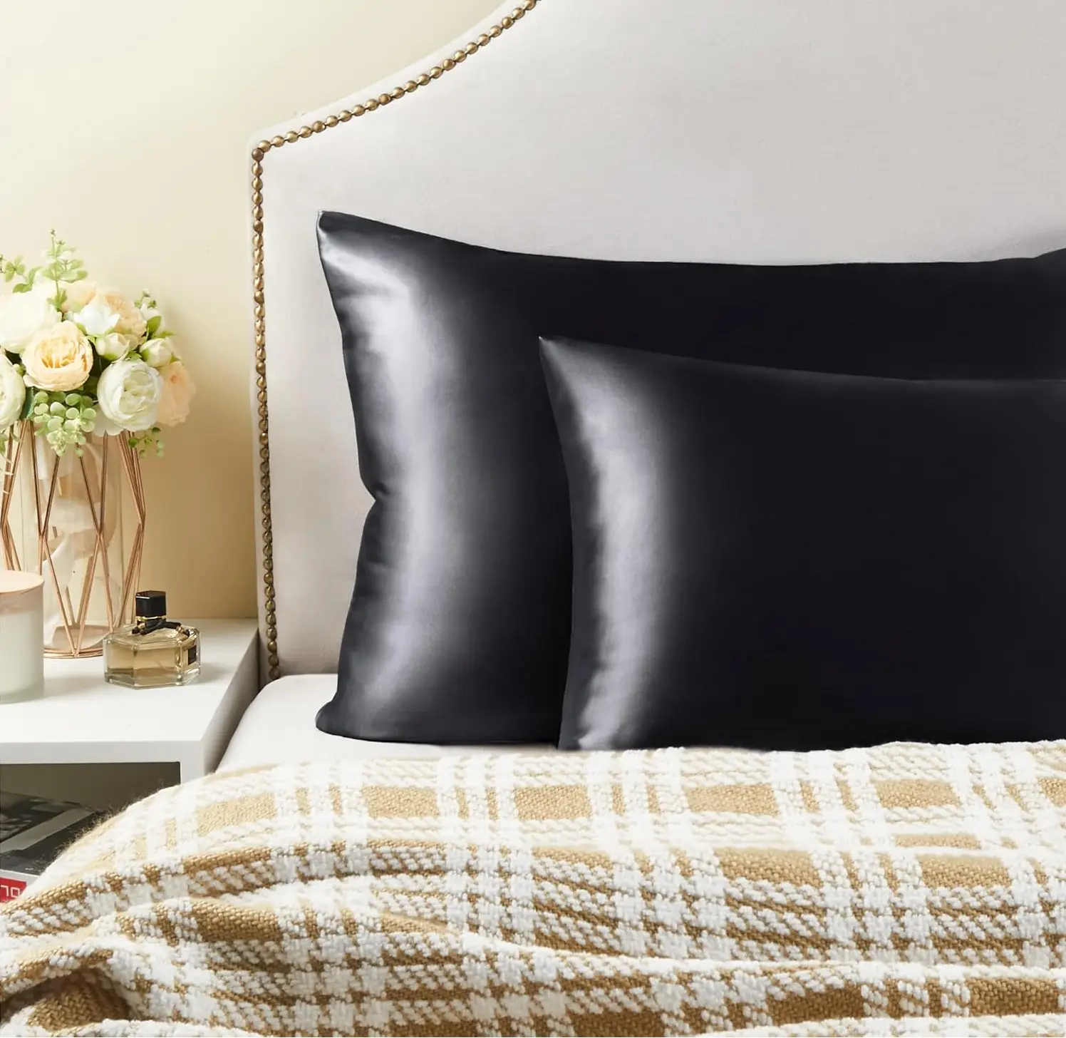 Fundas para almohada en satín negro con acabado brillante, sobre una cama con manta de cuadros beige y blanco.