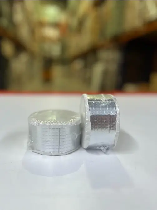 Set de dos rollos de cinta adhesiva impermeable gris con textura cuadriculada, envueltos en plástico transparente sobre superficie blanca.