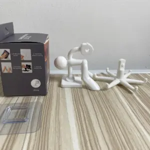 Gancho giratorio blanco de seis mordazas en caja, con base adhesiva transparente y figura humana decorativa sobre mesa de madera.