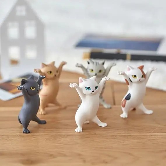 Cinco gatos decorativos en poses de baile con colores gris, naranja, blanco y tabby sobre un escritorio de madera.