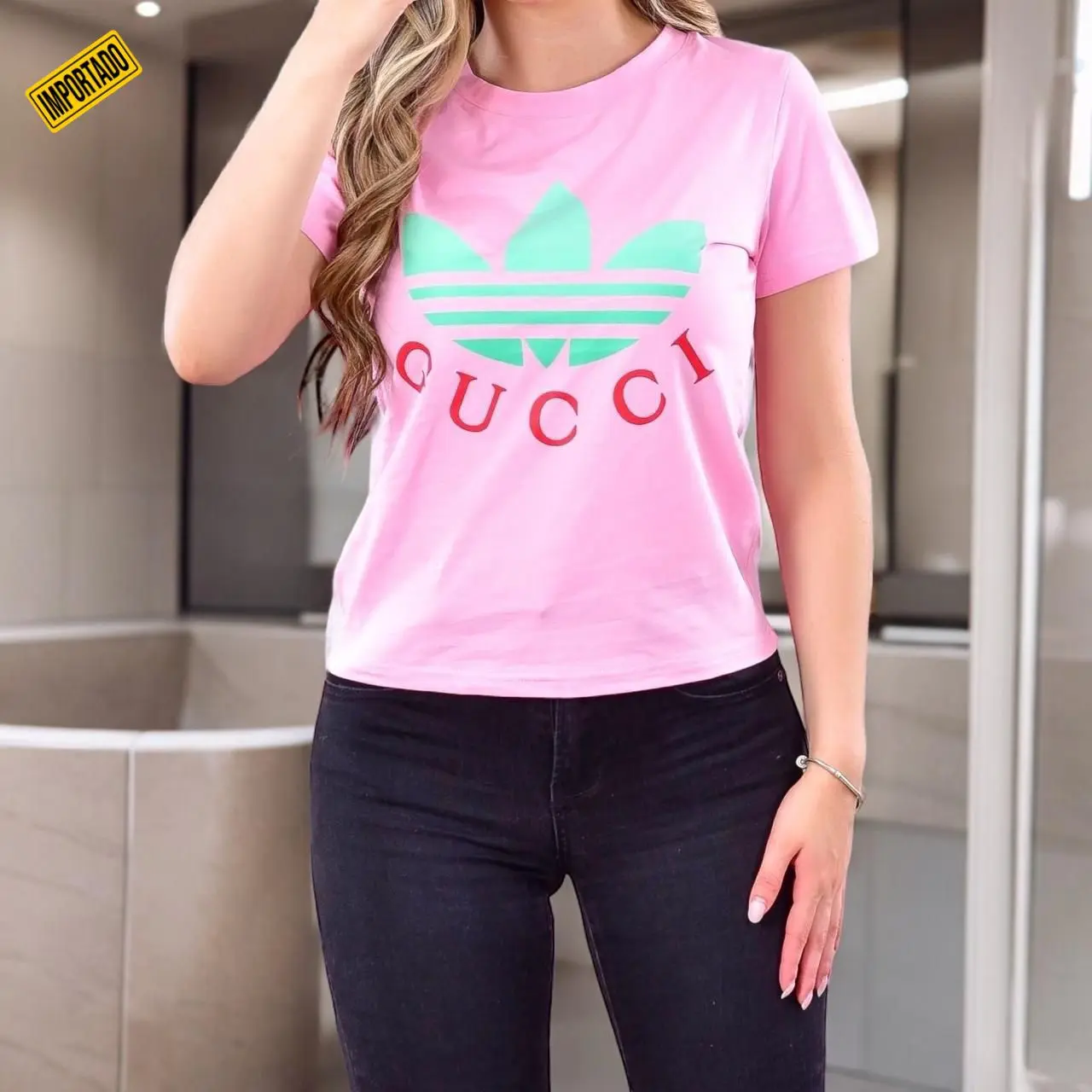 Camiseta casual rosa de tela fría con estampado verde y letras rojas, usada con jeans oscuros en plano frontal.