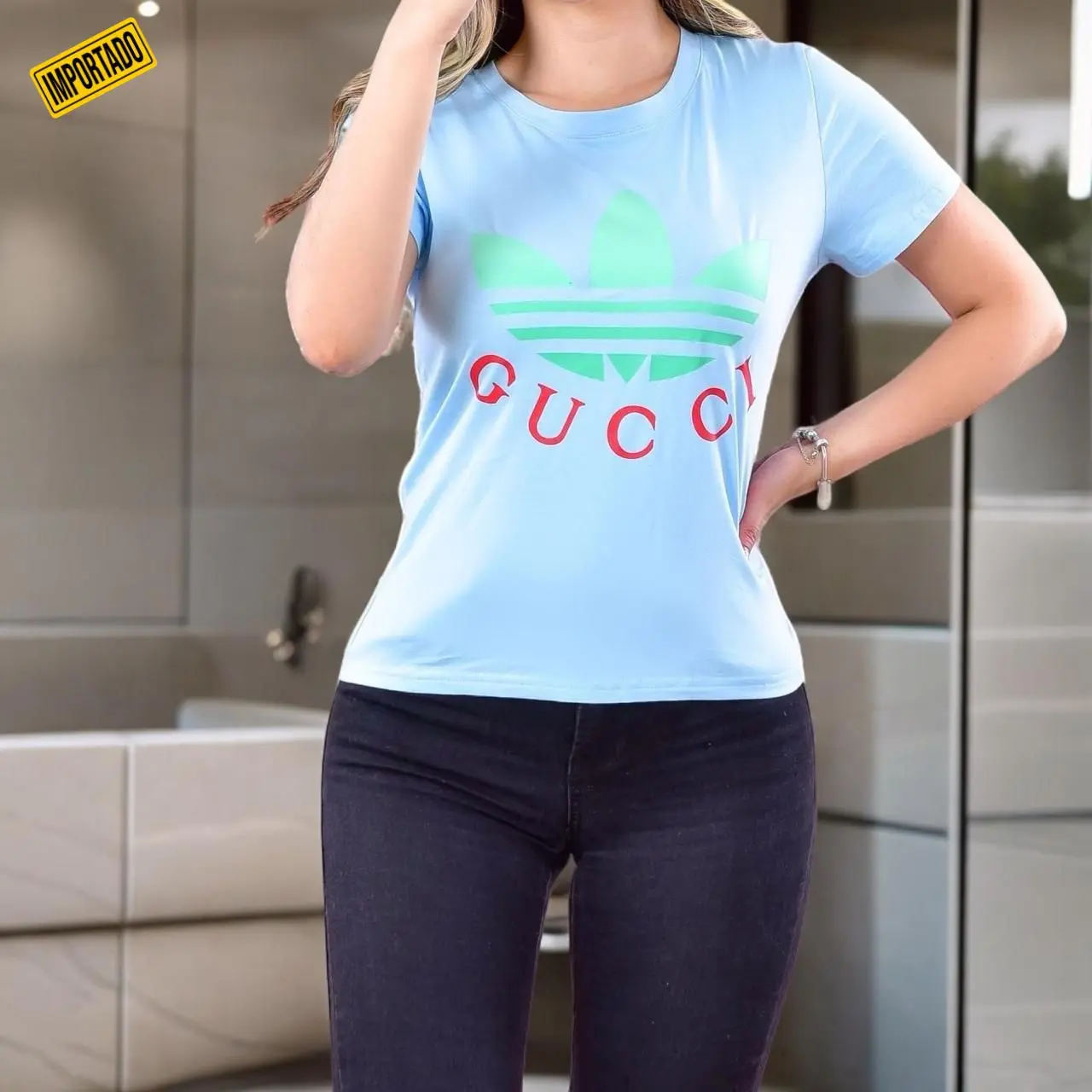 Camiseta casual celeste de tela fría para mujer con logotipo verde y rojo en el pecho, combinada con jeans oscuros.