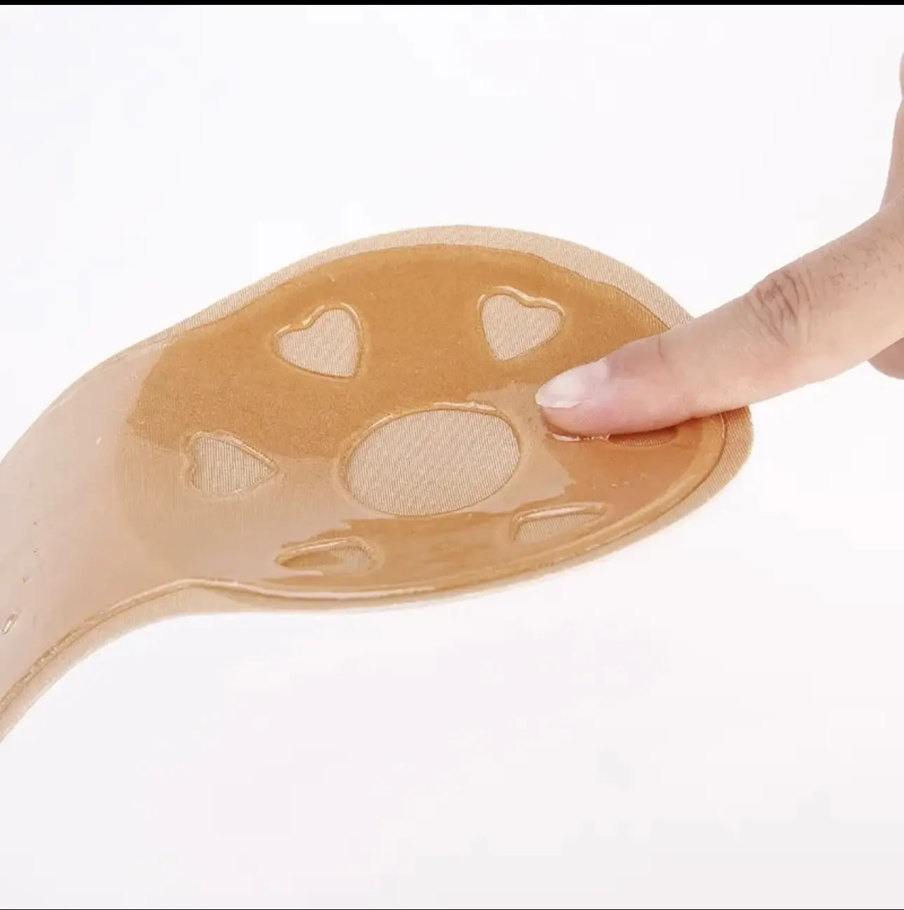 Brasier adhesivo color nude con interior de silicona brillante, diseño ergonómico con aberturas en forma de corazón y dedo presionando la textura pegajosa