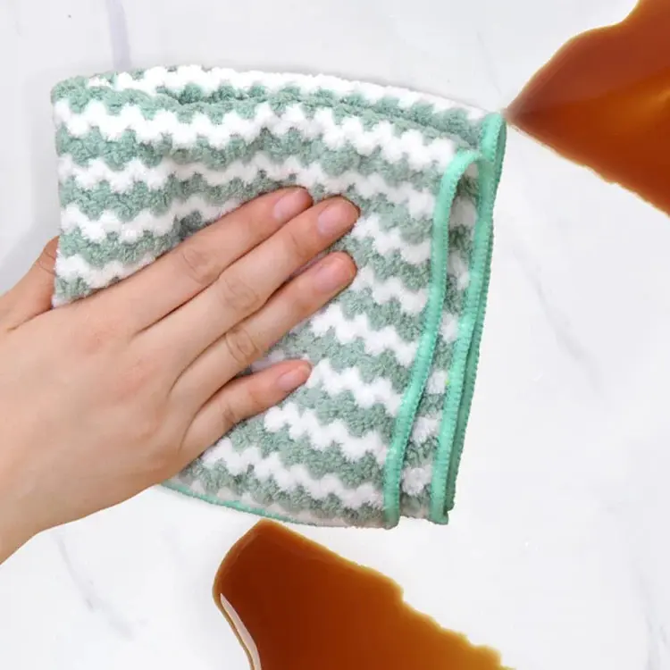 Paño de microfibra verde y blanco con diseño en zigzag limpiando un derrame de líquido marrón sobre superficie lisa.