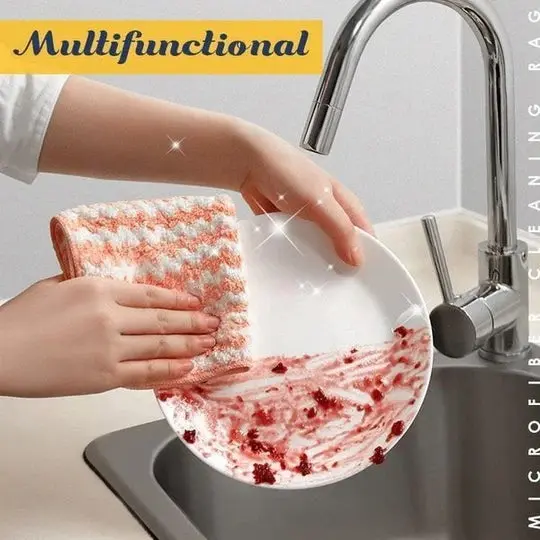 Paño de limpieza de microfibra color salmón con diseño texturizado, limpiando plato blanco con residuos de comida en lavaplatos.