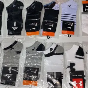 Doce pares de medias tobilleras en empaques individuales, con colores blanco, negro y gris de marcas como Nike, Adidas y Jordan.