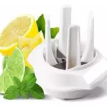 Cortadora de cítricos en cruz de plástico blanco con cuchillas verticales, junto a rodajas de limón, lima y hojas de menta fresca.