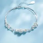 Brazalete plateado de tres hilos con esferas texturizadas y diseño delicado, con cierre ajustable y extensión sobre fondo azul claro.