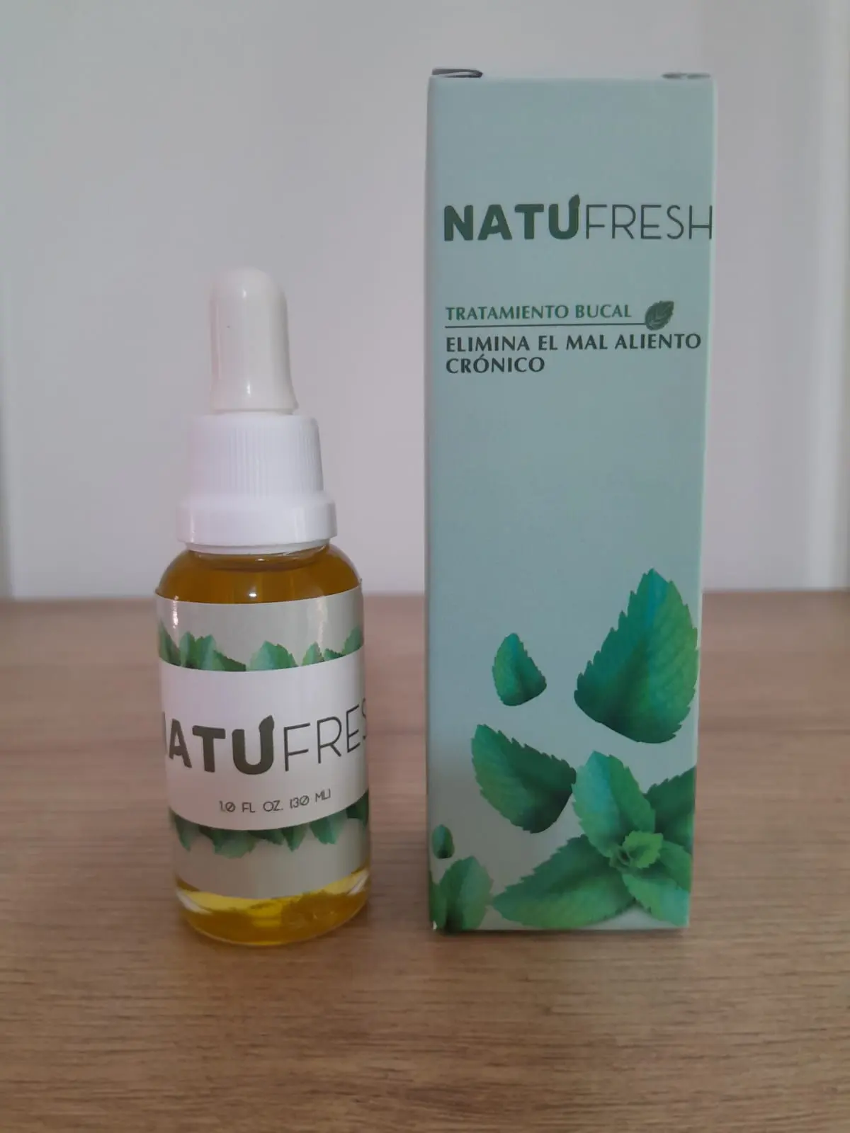 Frasco de 30 ml con gotero y caja azul claro de tratamiento bucal Natufresh con diseño de menta sobre superficie de madera.