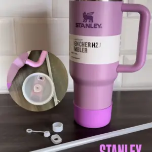 Termo Stanley violeta con asa y funda protectora, acompañado de un kit antiderrame de cinco piezas de silicona blanca y un sorbete sobre superficie oscura.