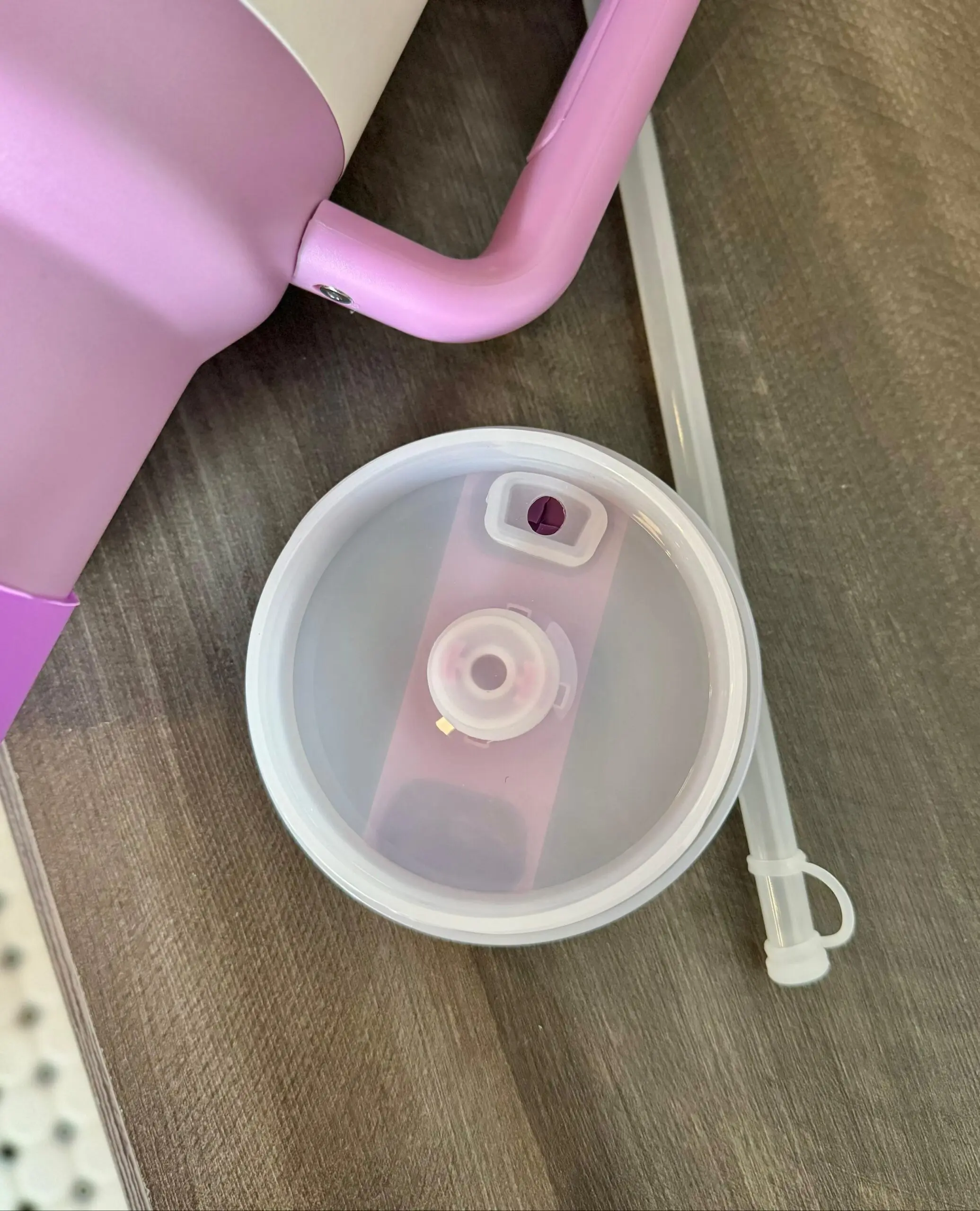 Tapa de termo Stanley rosa con válvula antiderrame desmontable, sorbete transparente y cuerpo parcial sobre superficie de madera.