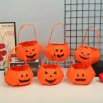 Set de cuatro bolsas naranjas de tela ligera para dulces de Halloween con rostros de calabaza y asas.