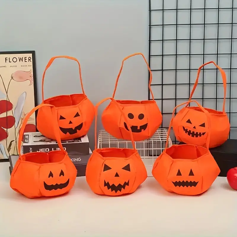 Set de cuatro bolsas naranjas de tela ligera para dulces de Halloween con rostros de calabaza y asas.