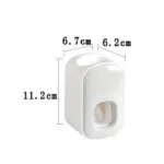 Dispensador de crema dental blanco de plástico brillante, medidas 11,2 cm de alto, 6,7 cm de profundidad y 6,2 cm de ancho, con botón pulsador frontal.