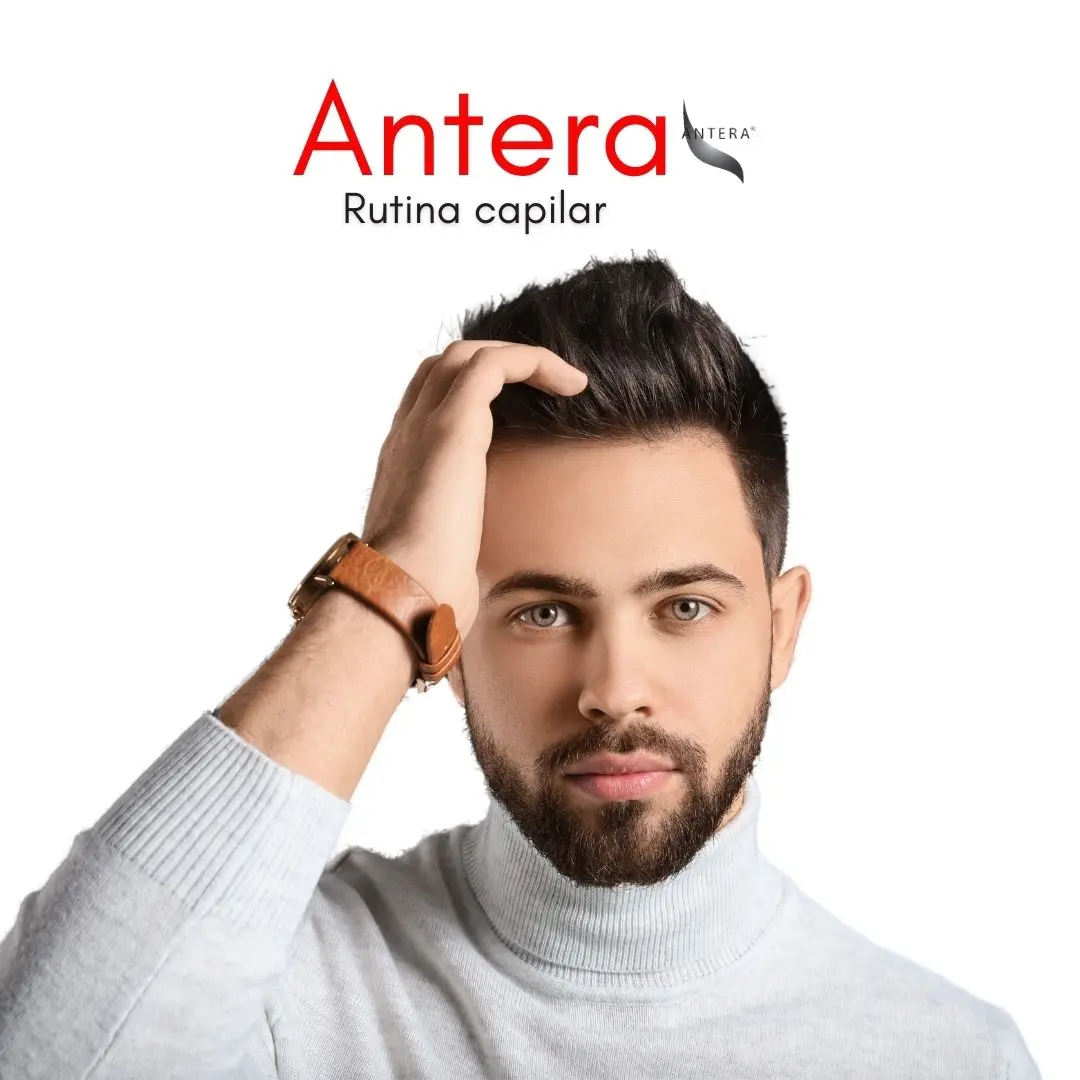 Hombre con barba y suéter gris claro tocándose el cabello oscuro, sobre fondo blanco, promocionando la rutina capilar anticaída Antera.