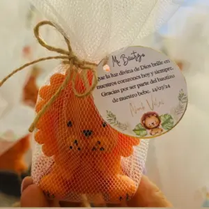 Vela artesanal de león color naranja en malla blanca con etiqueta personalizada de bautizo, ideal como recordatorio para fiestas temáticas de safari.