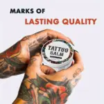 Bálsamo para tatuajes natural de 3.53 oz en tarro blanco con tapa ilustrada, sostenido por manos tatuadas mostrando hidratación de la piel.