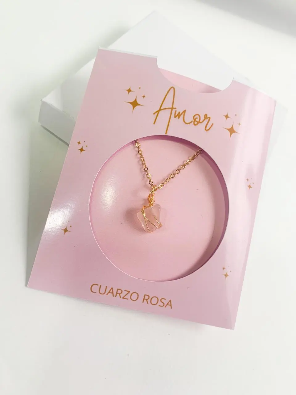 Collar de cadena dorada con dije de cuarzo rosa en caja decorativa rosa con detalles de estrellas y la inscripción Amor.
