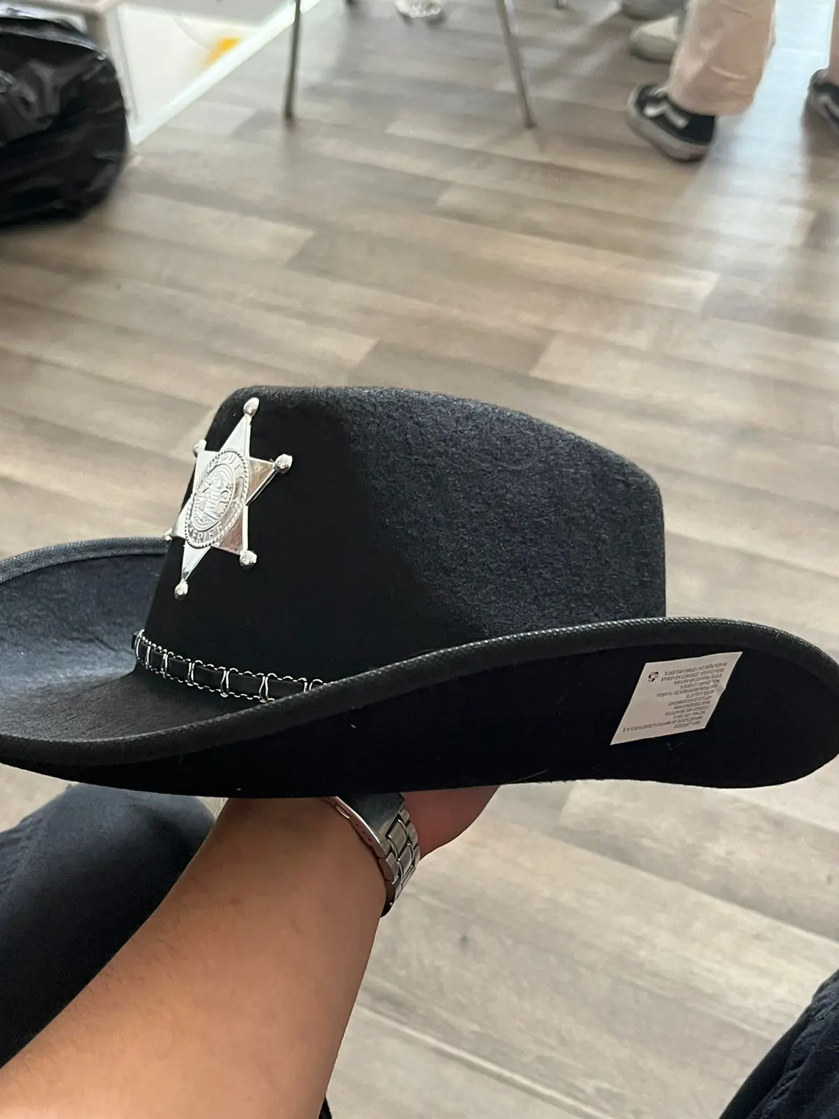 Sombrero de sheriff negro de fieltro con estrella plateada y banda trenzada, sostenido de perfil.