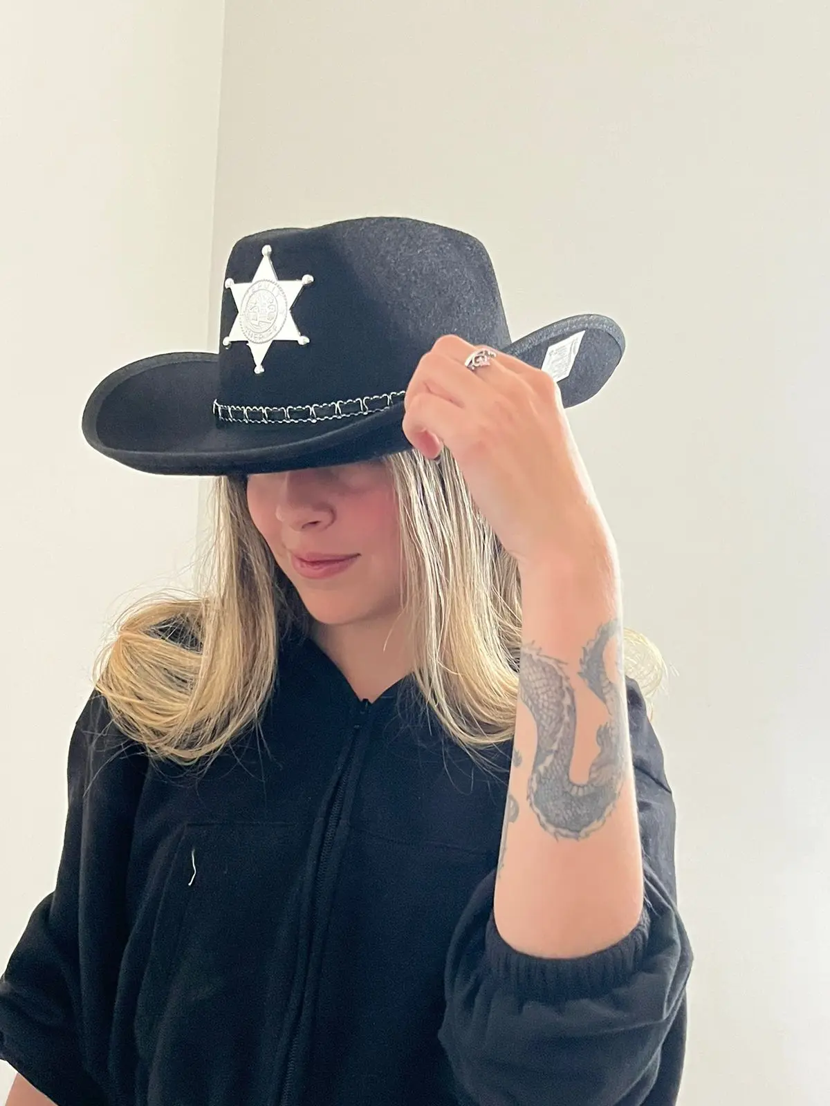 Sombrero de sheriff negro en fieltro con estrella plateada y cordón trenzado, usado por mujer rubia con sudadera oscura.