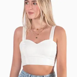Mujer rubia de perfil con crop top blanco de tirantes anchos y escote corazón, combinado con jeans claros.