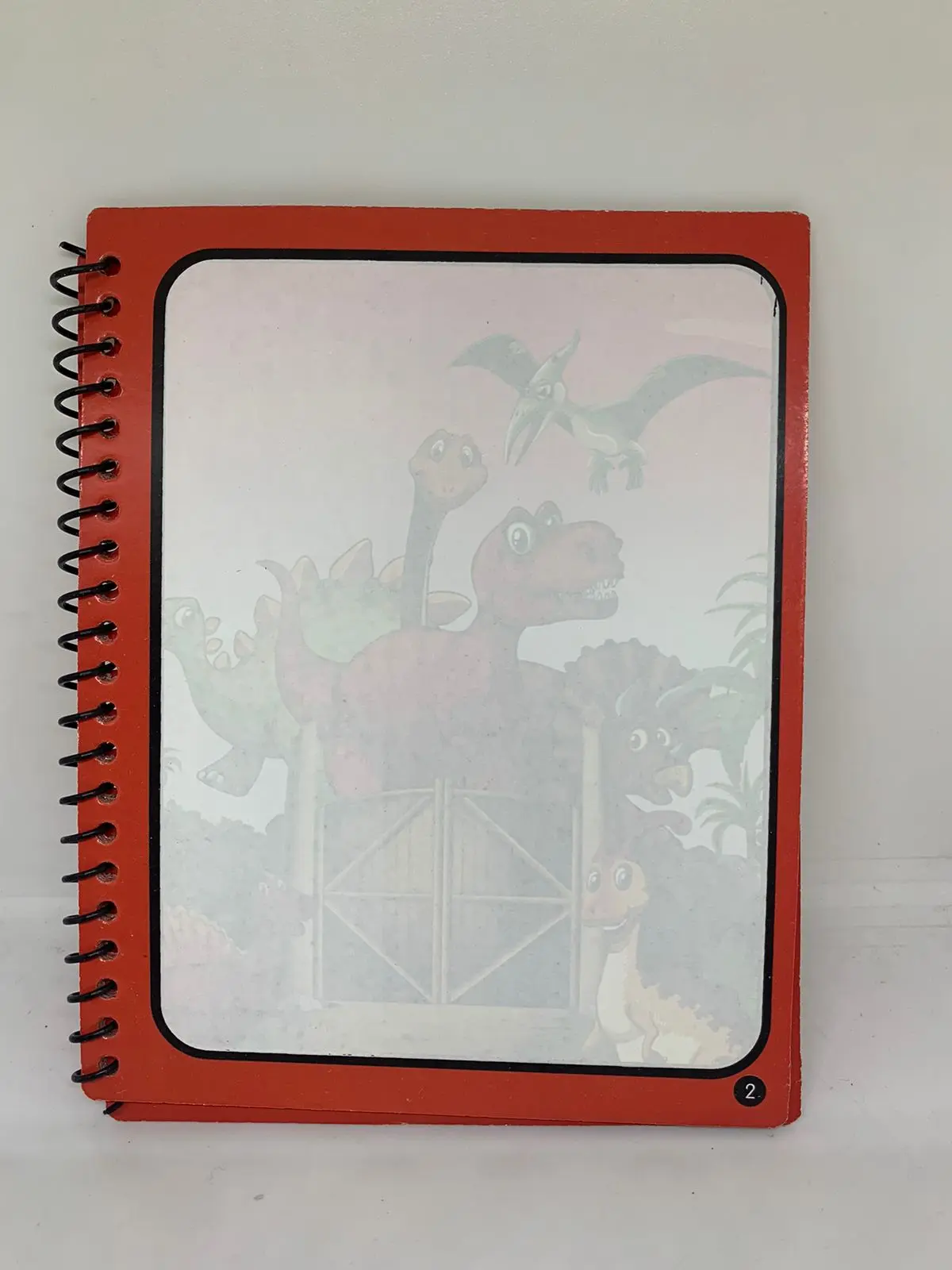 Libro de dibujo reutilizable con espiral roja y portada de dinosaurios animados en un paisaje prehistórico.