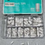 Caja organizadora con uñas postizas blancas de forma cuadrada en varios tamaños dispuestas en compartimentos transparentes.