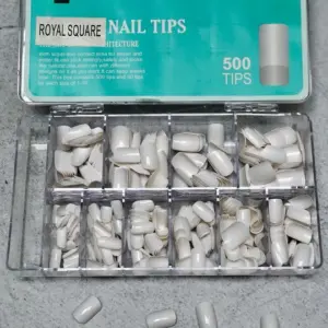Caja organizadora con uñas postizas blancas de forma cuadrada en varios tamaños dispuestas en compartimentos transparentes.