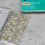 Caja de tips de uñas postizas transparentes Royal Square x500 organizados por tamaño y piezas sueltas sobre superficie gris.