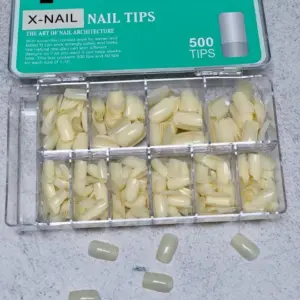 Caja organizadora con uñas postizas naturales en diez compartimentos y nueve piezas sueltas sobre superficie blanca, acabado marfil.
