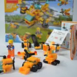 Set de bloques de construcción amarillos con caja, manual y modelos armados de bulldozer, avión y submarino junto a un muñeco trabajador.