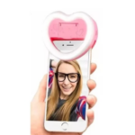 Aro de luz LED en forma de corazón color rosado con intensidad ajustable, montado en la parte superior de un smartphone sostenido por una mano.